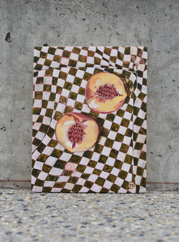 Two halves of a peach on a green and white checked table cloth. An original painting by West Australian artist Natasha Mott.
